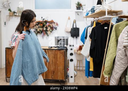 Eine Frau sucht in einer Boutique nach Kleidung, hält ein stilvolles Frühlingsgewand und denkt über einen neuen Look in einem gemütlichen Modegeschäft nach Stockfoto