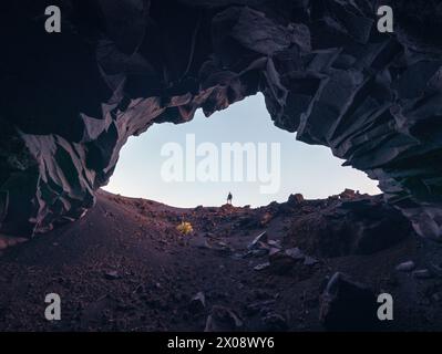 Ein einsamer Entdecker steht an der Mündung einer zerklüfteten Höhle mit Blick auf vulkanisches Gelände auf La Palma Island, Spanien, unter klarem Himmel in der Abenddämmerung Stockfoto