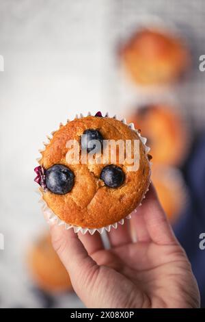 Nahaufnahme einer Hand, die einen köstlichen Heidelbeermuffin mit sichtbaren Beeren vor einem verschwommenen Hintergrund hält Stockfoto