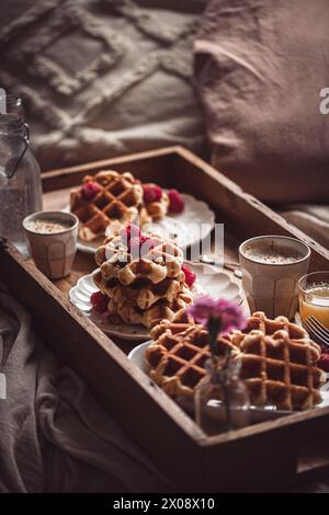 Ein warmes und einladendes Frühstück mit frisch gebackenen Waffeln mit Himbeeren, Kaffee und Saft, serviert auf einem Holztablett im Bett Stockfoto