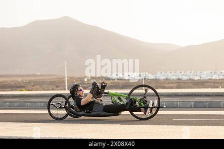 Seitenansicht einer Sportlerin beim Handradtraining auf einer Straße mit Bergen im Hintergrund. Stockfoto