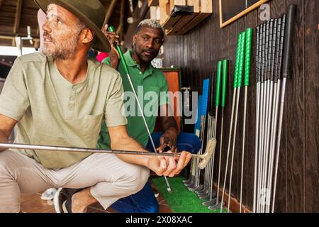 Zwei Männer, ein Kaukasier und ein Afroamerikaner, wählen Putter aus einem Rack auf einem Minigolfplatz aus und bereiten sich auf ein Freundschaftsspiel vor. Stockfoto