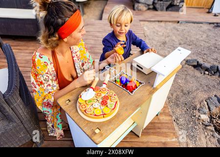 Eine Mutter und ein Sohn genießen das Leben eines Transporters mit Terrasse, Garten und Wohnkomfort, einschließlich einer provisorischen Küche für spielerische Kochaktivitäten. Stockfoto