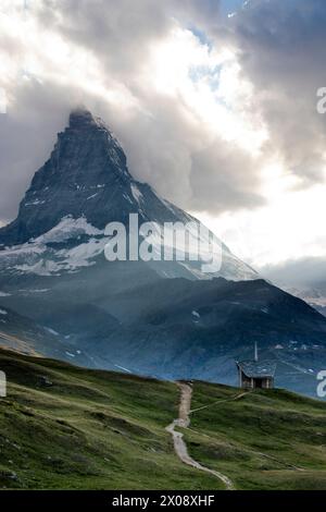 Eine einsame Berghütte steht vor dem legendären Matterhorn, das in den goldenen Tönen des Sonnenuntergangs gekleidet ist, mit freiem Blick auf den Vollmond, der im SWI aufgeht Stockfoto