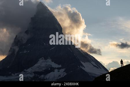 Wanderer stehen in Silhouette vor der Weite der Schweizer Alpen, mit dem legendären Matterhorn majestätisch in den Sonnenuntergang beleuchteten Himmel Stockfoto