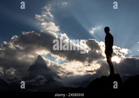 Die markante Silhouette eines einsamen Wanderers liegt vor dem strahlenden Himmel bei Sonnenuntergang und das Matterhorn im Hintergrund, das Abenteuer und symbolisiert Stockfoto