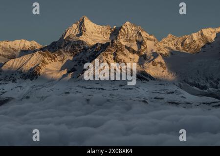Ein ruhiger Sonnenaufgang taucht den Gipfel des Matterhorns in ein warmes Licht über einem Wolkenmeer und schafft eine atemberaubende Alpenlandschaft Stockfoto