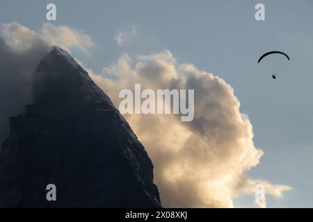 Eine Silhouette eines einsamen Gleitschirms, der vor der dramatischen Kulisse des Matterhorns in der Dämmerung von wirbelnden Wolken umschwebt Stockfoto