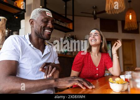 Zwei Freunde lachen und spielen ein Ratespiel mit Haftnotizen auf der Stirn in einer Bar Stockfoto