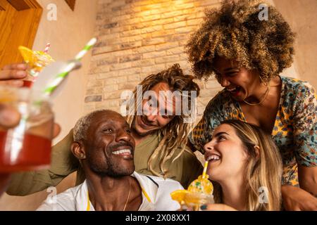 Eine vielfältige Gruppe fröhlicher Freunde lacht und tröstet Getränke in einer warm beleuchteten Bar, die die Freude an Freundschaft zum Ausdruck bringt Stockfoto