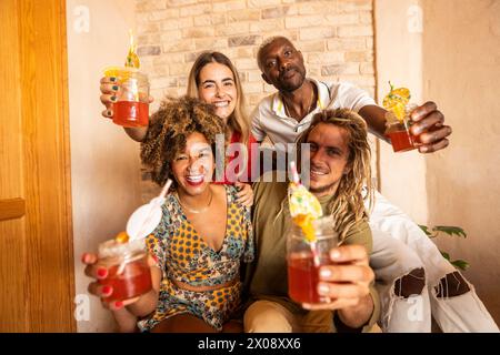 Eine fröhliche Gruppe von Freunden aus verschiedenen Ethnien hält bunte Getränke mit Beilagen und tobt fröhlich an und feiert gemeinsam in einer Bar Stockfoto