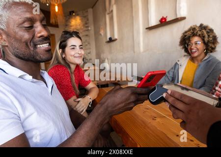 Eine vielfältige Gruppe von Freunden genießt eine gute Zeit zusammen, lacht und interagiert mit einem Smartphone in einer rustikalen Bar Stockfoto