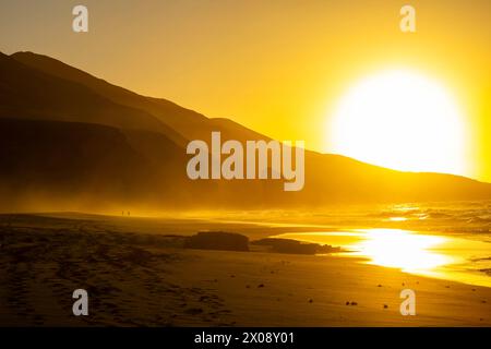 Ein goldener Sonnenuntergang strahlt einen lebendigen Glanz über die weitläufigen Sandstrände von Cofete mit den Silhouetten der Berge auf Fuerteventura aus Stockfoto