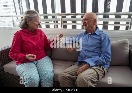 Ein älteres Ehepaar sitzt bequem auf einem Sofa und teilt eine angenehme Unterhaltung in einem gemütlichen, gut beleuchteten Zimmer. Stockfoto