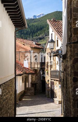 Enge kopfsteingepflasterte Straße in Potes, Kantabrien, mit traditionellen Steinhäusern und den Bergen von Picos de Europa im Hintergrund. Stockfoto