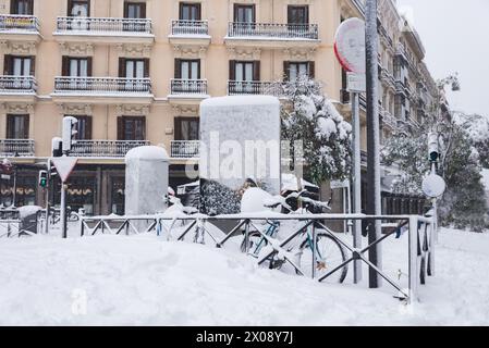 Schneebedeckte Fahrräder und Lampenpfosten säumen eine Straße von Madrid inmitten eines seltenen Schneefalls und zeigen eine wunderschöne Winterszene in einer belebten Stadt. Stockfoto