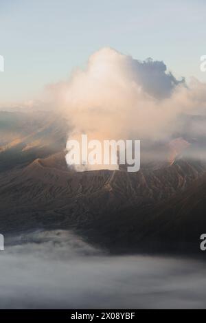 Ein majestätischer vulkanischer Berg bricht Rauchschwaden im Morgenlicht aus, das in Nebel gehüllt ist Stockfoto