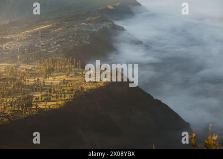 Der Sonnenaufgang erleuchtet das indonesische Hochland mit einem dicken Nebel, der durch die Täler zwischen Terrassenfeldern fließt Stockfoto