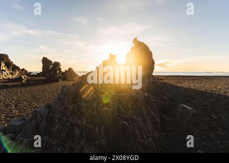 Ein fesselnder Sonnenaufgang führt durch die einzigartigen Felsformationen an einem isländischen Kiesstrand und sorgt für einen dramatischen Start in den Tag Stockfoto