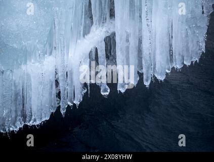 Atemberaubende Aussicht auf majestätische Eiszapfen, die von einer Klippe mit dunkler felsiger Kulisse herabhängen und die kalte Schönheit eines isländischen Winters zeigen Stockfoto