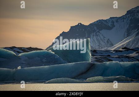 Fangen Sie die ruhige Schönheit der Gletscherlagune von Jokulsarlon in Island ein, mit sanftem goldenem Stundenlicht, das die schwimmenden Eisberge gegen einen majestätischen Anblick beleuchtet Stockfoto