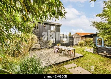 Ein modernes schwarzes Haus mit einer großen Holzterrasse mit Esstisch und einem üppigen Garten umgeben von Bambus. Stockfoto