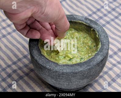 Guacamole in Molcajete (traditioneller mexikanischer Mörtel und Stößel zum Mahlen von Gewürzen und zum Herstellen von Soßen) scharfer Avocado-Dip mit aztekischen Wurzeln auf gestreiften Streifen Stockfoto