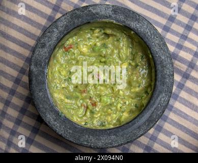 Guacamole in Molcajete (traditioneller mexikanischer Mörtel und Stößel zum Mahlen von Gewürzen und zum Herstellen von Soßen) scharfer Avocado-Dip mit aztekischen Wurzeln auf gestreiften Streifen Stockfoto