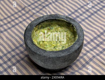 Guacamole in Molcajete (traditioneller mexikanischer Mörtel und Stößel zum Mahlen von Gewürzen und zum Herstellen von Soßen) scharfer Avocado-Dip mit aztekischen Wurzeln auf gestreiften Streifen Stockfoto