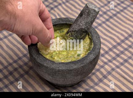 Guacamole in Molcajete (traditioneller mexikanischer Mörtel und Stößel zum Mahlen von Gewürzen und zum Herstellen von Soßen) scharfer Avocado-Dip mit aztekischen Wurzeln auf gestreiften Streifen Stockfoto