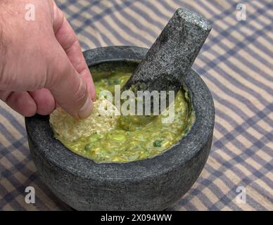 Guacamole in Molcajete (traditioneller mexikanischer Mörtel und Stößel zum Mahlen von Gewürzen und zum Herstellen von Soßen) scharfer Avocado-Dip mit aztekischen Wurzeln auf gestreiften Streifen Stockfoto