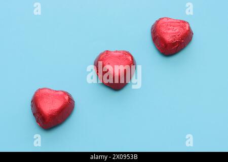 Drei herzförmige Pralinen in roter Folie, Draufsicht. Stockfoto