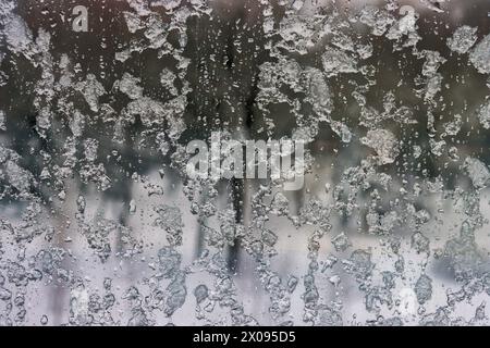 Gefrorener Regen fällt auf ein Fenster mit einem verschwommenen schneebedeckten Blick. Eis und Wasser auf dem Fenster in Nahaufnahme. Stockfoto