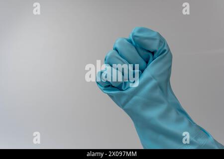 Frauenhand in türkisfarbenen Gummihandschuhen, die eine Faustgeste auf weißem Hintergrund macht. Konzept für Reinigung, Hausarbeit und Hygiene. Stockfoto