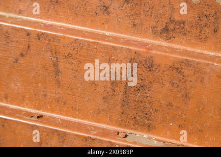 Abblätternde Lackschicht an einer schmutzigen und alten orangefarbenen Metalltür. Abstraktes Nahbild einer wetterbeschädigten Außentür. Stockfoto