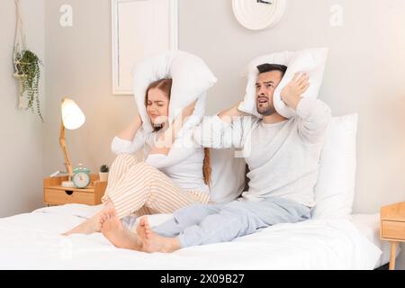 Junges Paar mit Kopfkissen, die von lauten Nachbarn im Schlafzimmer litten Stockfoto