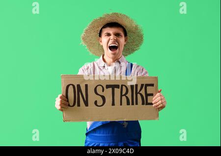 Protest gegen männlichen Landwirt, der ein Plakat mit STREIKTEXT vor grünem Hintergrund hält Stockfoto