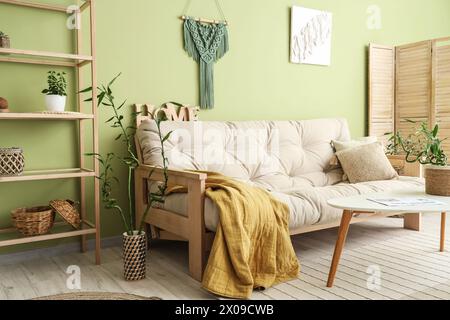 Stilvolle Einrichtung mit grünem Wohnzimmer mit Bambusstämmen und gemütlichem Sofa Stockfoto