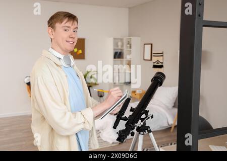 Männlicher Student mit Teleskop-Schrift im Copybook zu Hause Stockfoto