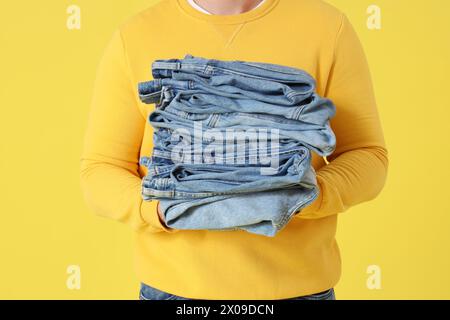 Junger Mann mit einem Stapel Jeans auf gelbem Hintergrund, Nahaufnahme Stockfoto