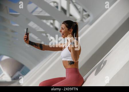 Lächelnde Athletin macht Selfie auf einem Smartphone nach dem Morgenlauf im Freien und zeigt Bizeps Stockfoto