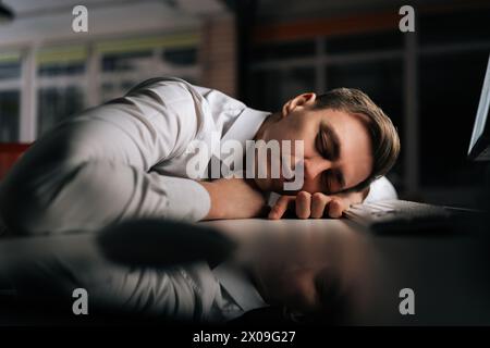 Nahaufnahme eines müden, verschlafenen männlichen Angestellten, der spät in der Nacht auf dem Schreibtisch schläft. Erschöpfter Geschäftsmann, der während der Arbeit mit dem Kopf auf der Tastatur schläft Stockfoto