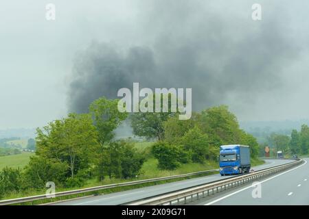 Eine beträchtliche Menge schwarzen Rauches, der von der Seite einer stark befahrenen Autobahn in den Himmel strömt, was wahrscheinlich auf einen schweren Vorfall oder einen Brand hinweist. Stockfoto