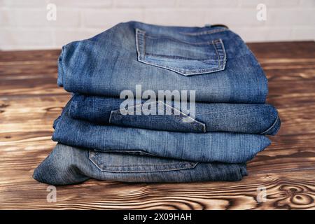 Ein hübscher Haufen Jeans auf einem rustikalen Holztisch, in dem Denim-Kleidung in einem schlichten Ambiente präsentiert wird. Stockfoto