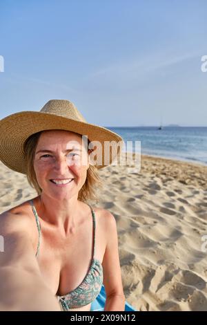 Eine Frau mittleren Alters mit macht ein Selfie am Strand mit ihrem Smartphone Stockfoto