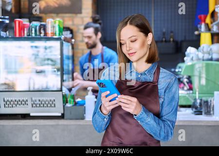 Junge Dienstarbeiterin auf der Schürze mit Smartphone im Restaurant, im Café Stockfoto