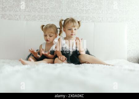 Zwei junge Mädchen sitzen auf einem Bett, die Hände in einer fröhlichen Geste in der Luft hochgehoben. Stockfoto