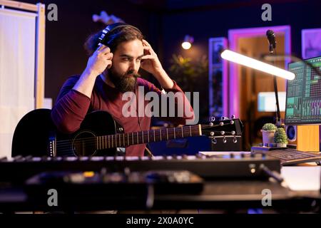 Sound-Komponist, der mit elektronischer Einrichtung im Heimstudio arbeitet und akustische Gitarrenmelodien aufnimmt und abspielt. Musiker, der mit Signalverarbeitungstechniken und Audiosteckern am Schreibtisch arbeitet. Stockfoto