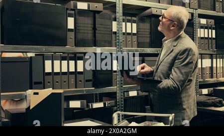 Privatdetektiv sucht nach Akten basierend auf Fallnamen im Archiv, sucht nach Rechtsdokumenten und Verschlusssachen auf dem Laptop. Agent arbeitet an Kriminologie im Vorfallsraum. Kamera B.. Stockfoto