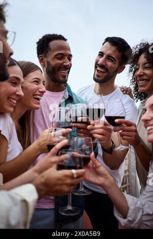 Vertikal. Treffen verschiedener fröhlicher Freunde, tosten Rotwein und feiern eine Geburtstagsparty Stockfoto